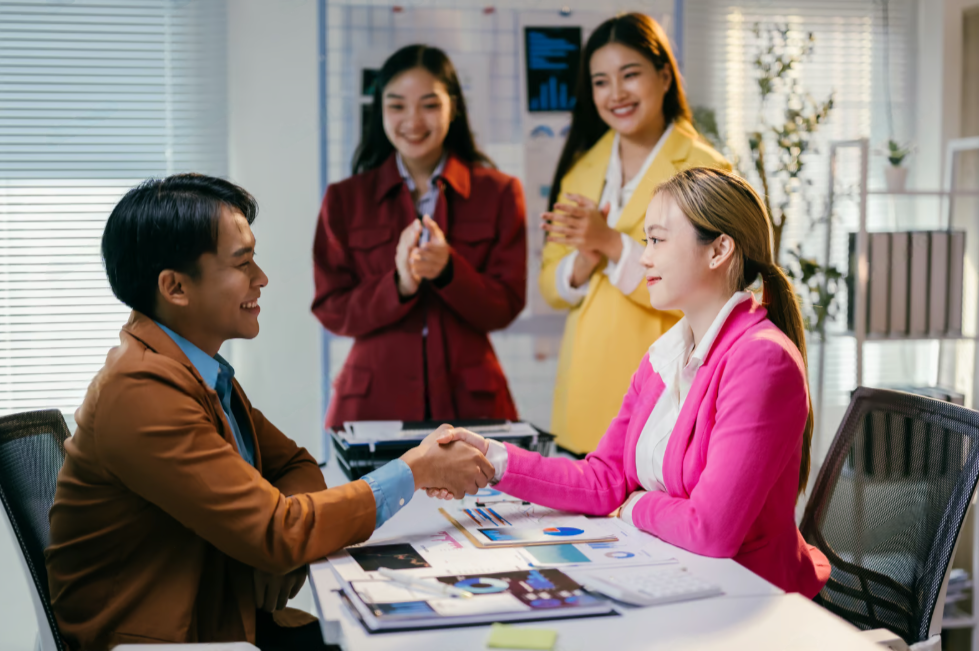 In a boardroom, an Asian team meets at a desk, presenting financial terms